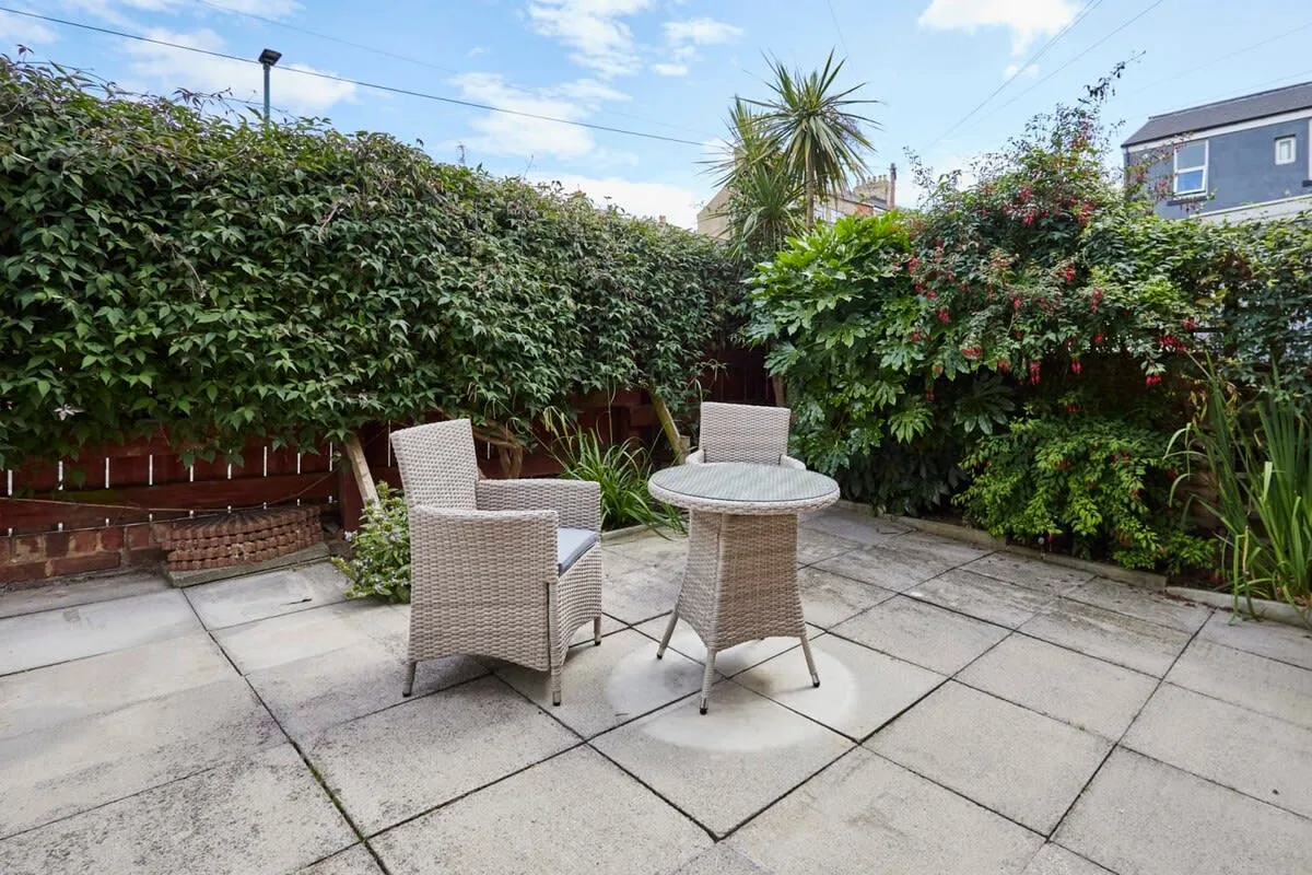 A paved garden patio with wicker seating and a round table.