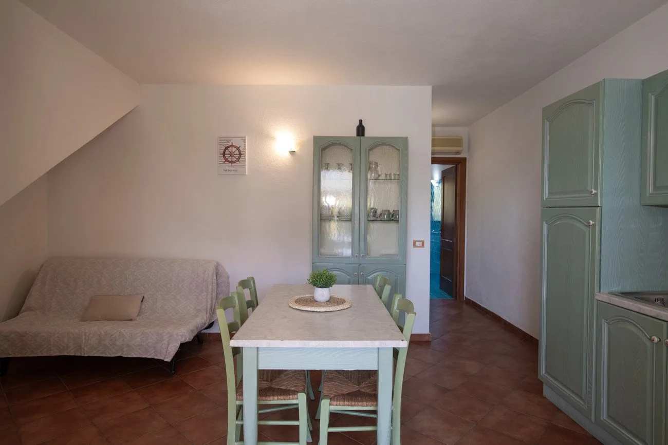 Un comedor con mesa y sillas, junto a un sofá y armarios verdes.