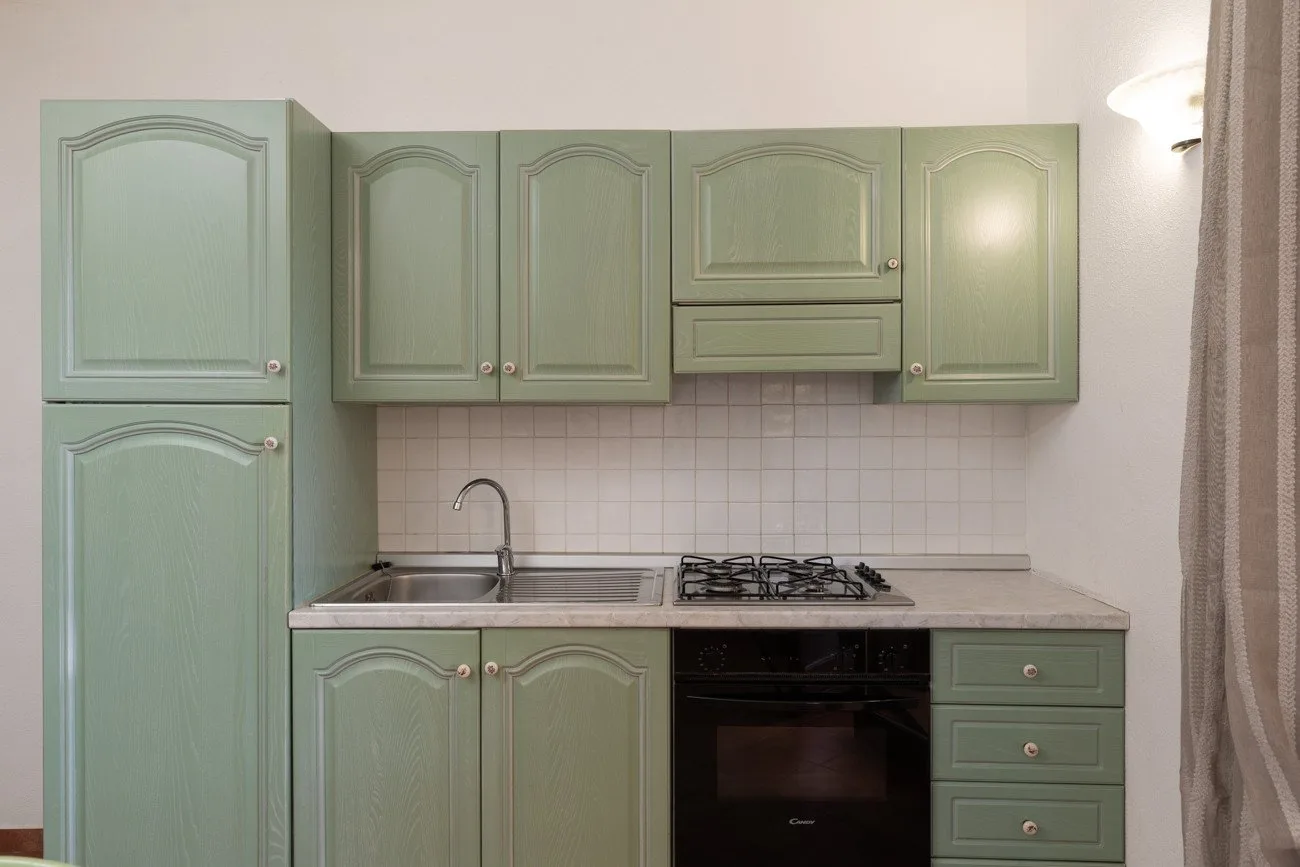 Una cocina compacta con gabinetes verde salvia, fregadero y placa de cocina.