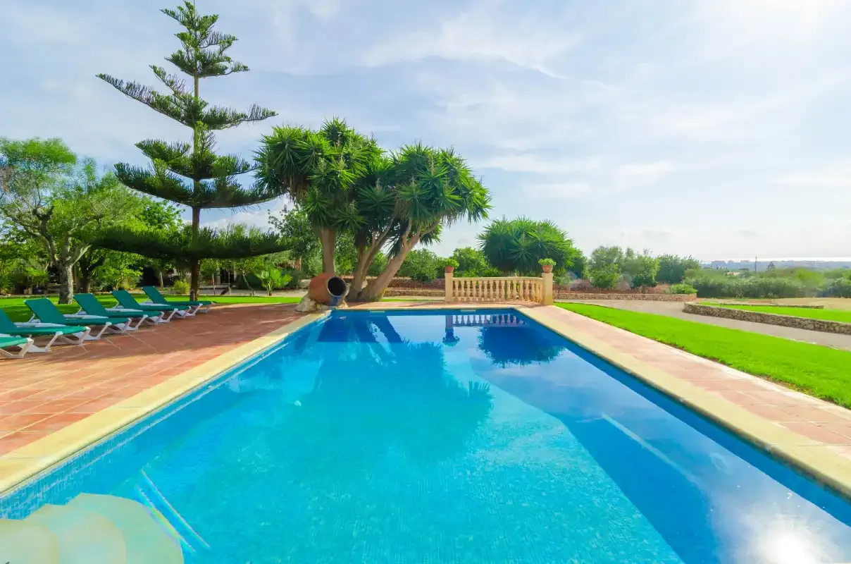 Una piscina al aire libre rodeada de patios pavimentados y césped verde.