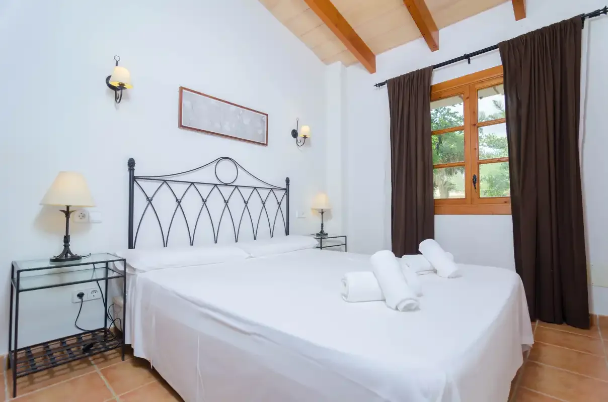 Un dormitorio con una cama blanca, un cabecero de metal negro y una ventana con cortinas.