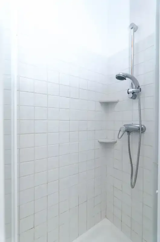 Una ducha alicatada con una ducha de mano y estantes en la pared.