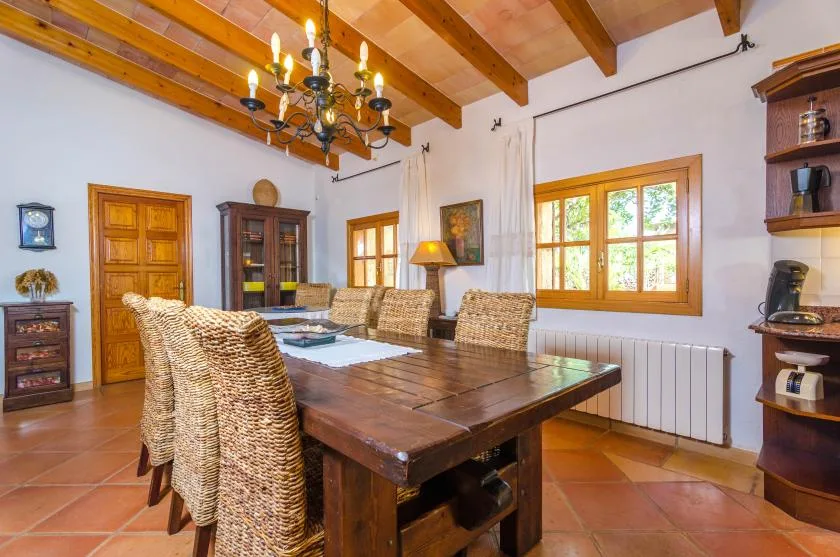 Un comedor con una mesa de madera, asientos tejidos y una ventana grande.