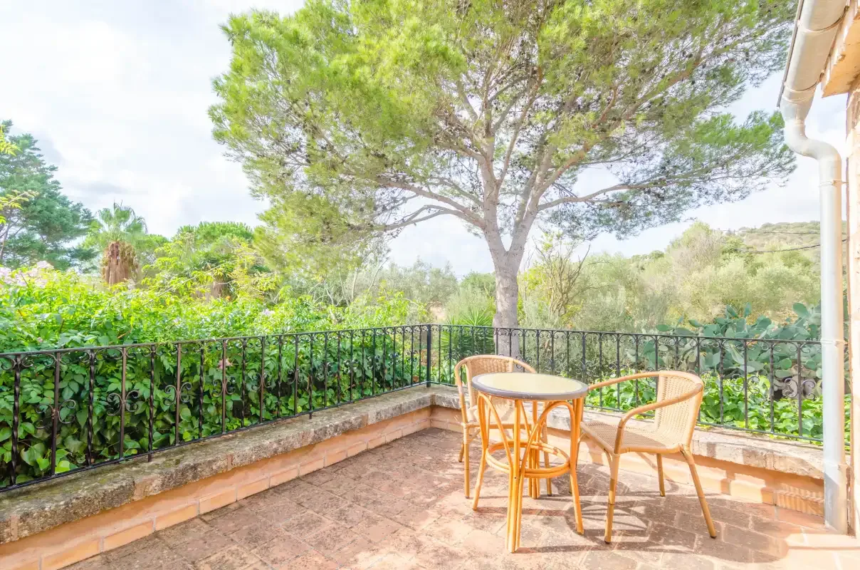 Una terraza exterior de baldosas tiene una mesa pequeña y asientos junto a una barandilla de jardín.
