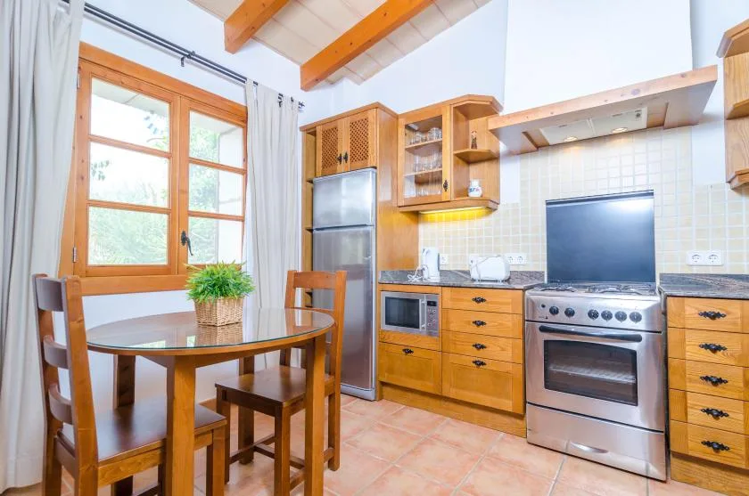 Una cocina con armarios de madera, una estufa y una mesa de comedor junto a la ventana.