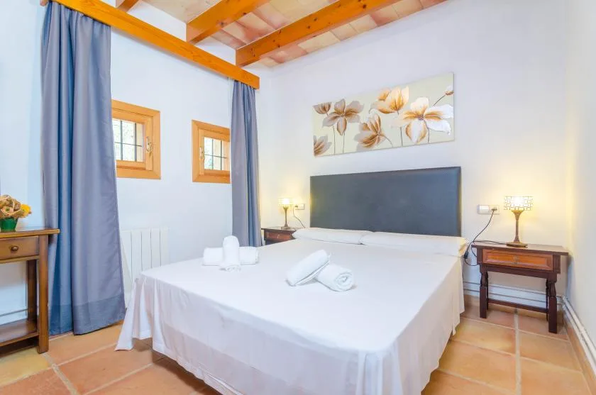 Un dormitorio con una cama bien tendida, mesillas de noche y arte floral en la pared.