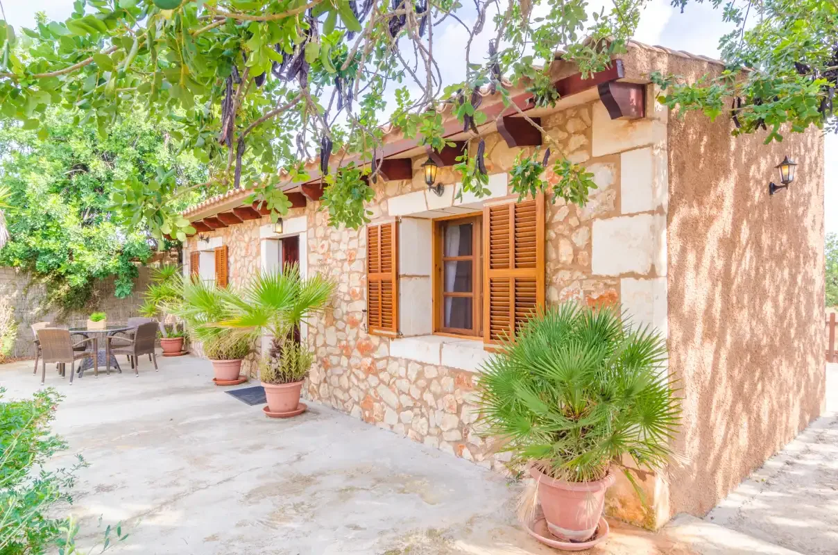 El exterior de una casa de piedra da a un patio pavimentado con asientos y plantas en macetas.
