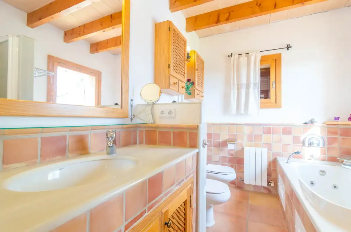 Un baño alicatado con lavabo, inodoro y bañera bajo vigas de madera vistas.