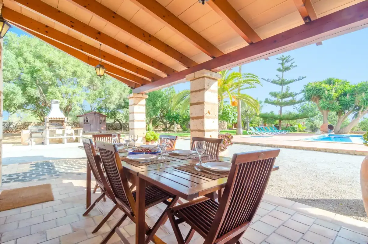 Un patio cubierto tiene una mesa de comedor y asientos junto a una piscina.