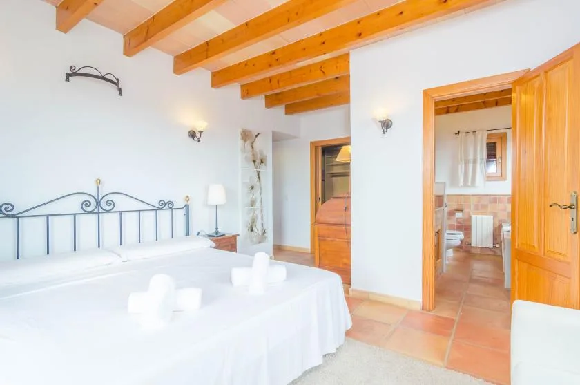 Un dormitorio luminoso con una cama tendida y vigas de madera expuestas en el techo.