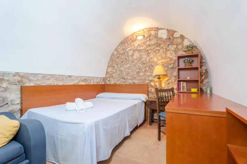 Un dormitorio con una cama doble, un escritorio y una estantería junto a una pared de piedra.