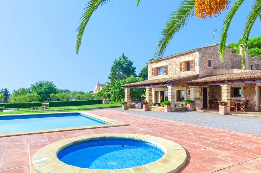 Una casa de piedra da a un patio embaldosado con piscina y spa circular.