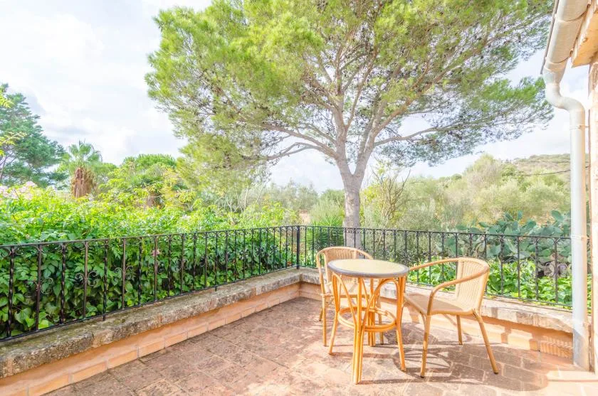 Una terraza exterior soleada con una mesa pequeña y asientos junto a un jardín.