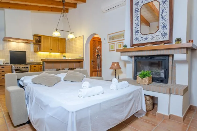 Un dormitorio con una cama bien arreglada, una chimenea y una cocina al fondo.