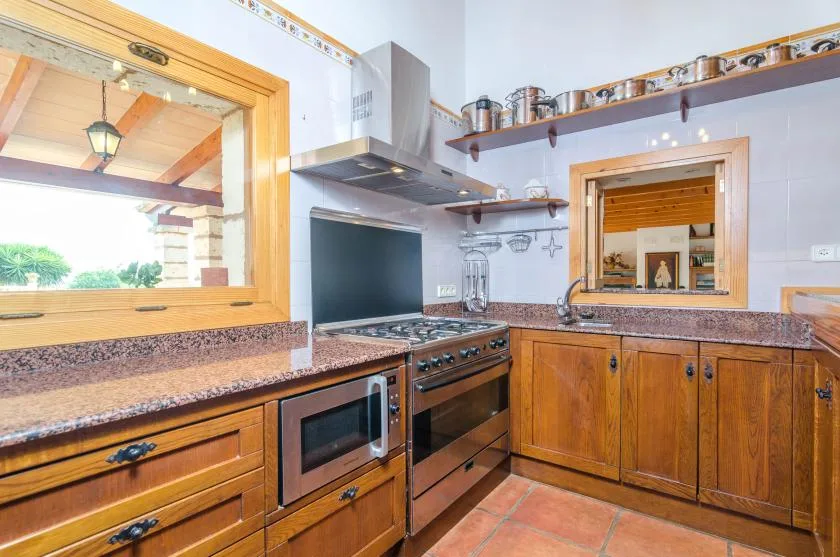 Una cocina con armarios de madera, una placa de cocción y una ventana con vistas a la vegetación.