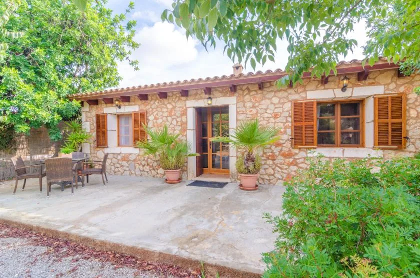 Exterior de una casa de piedra con ventanas con contraventanas, patio y palmeras en macetas.