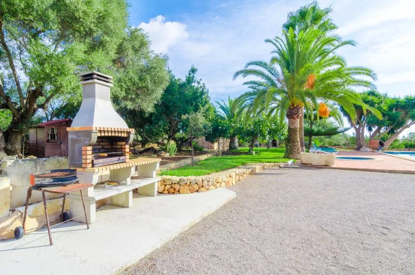 Una zona de barbacoa al aire libre con parrilla, asientos y palmeras.