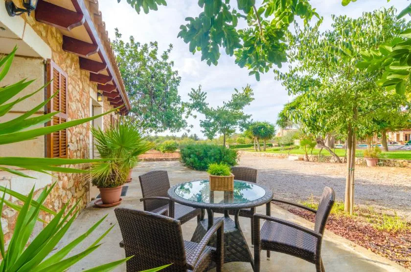 Un patio al aire libre con una mesa redonda y asientos da a un jardín ajardinado.