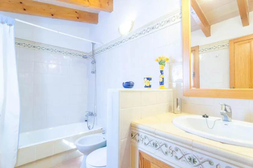 Un baño alicatado con bañera, inodoro y lavabo bajo un espejo grande.