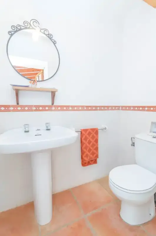 Un baño con lavabo de pedestal, inodoro y toalla naranja.