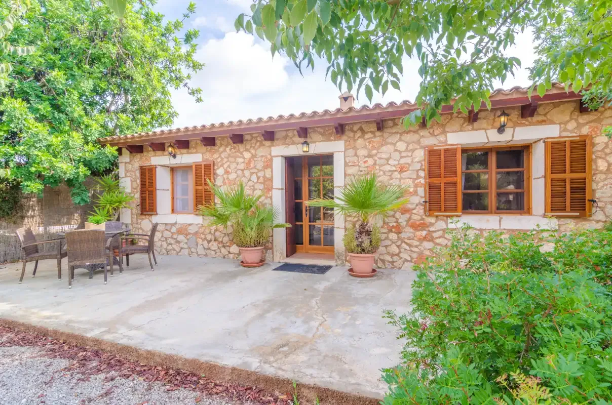Una casa de piedra da a un patio pavimentado con asientos al aire libre y plantas.