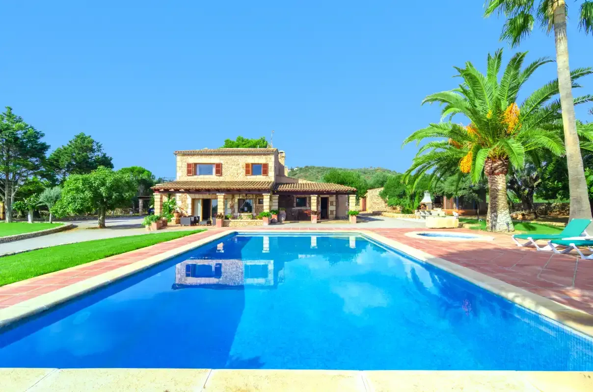 Una piscina frente a una casa, con palmeras y tumbonas cerca.