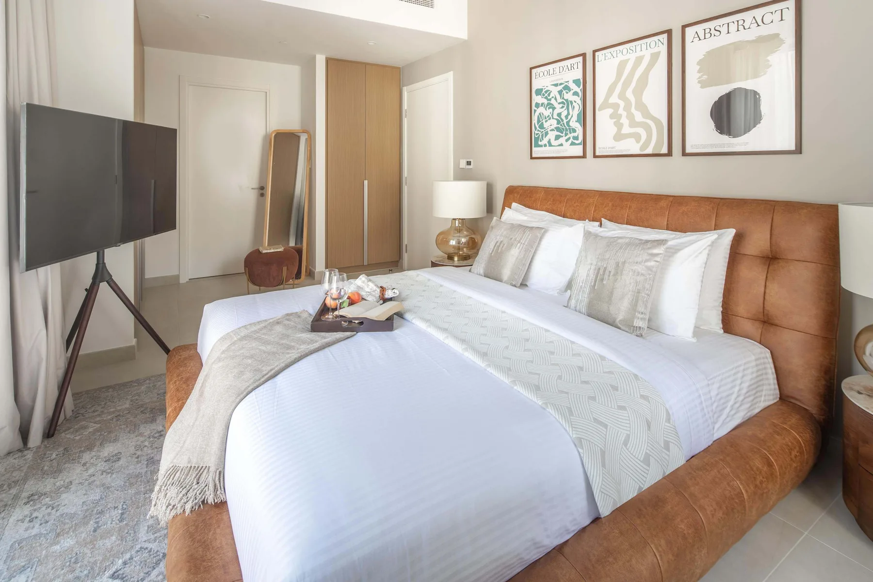Un dormitorio con una cama grande, ropa de cama blanca y láminas enmarcadas en la pared.