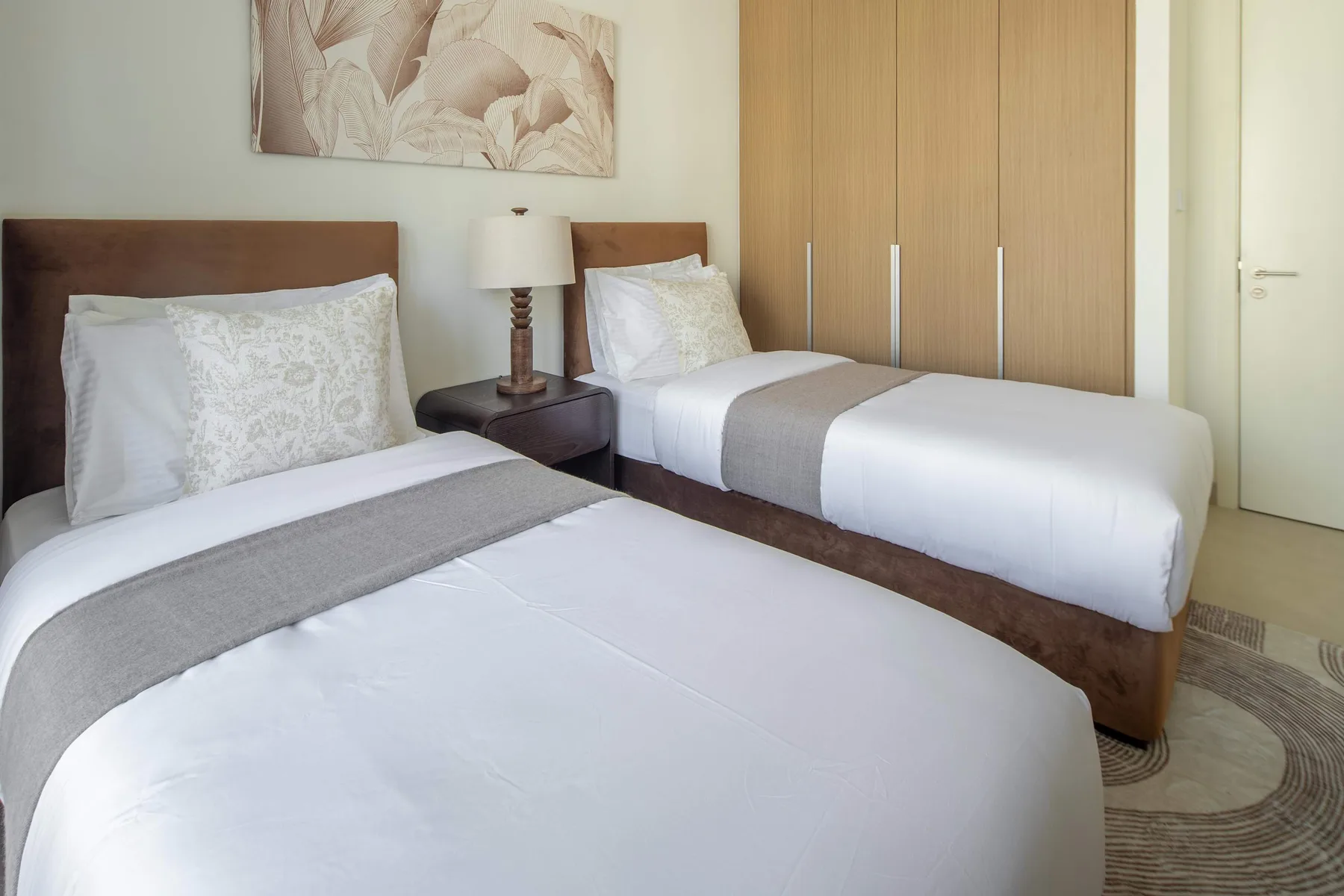 Un dormitorio con dos camas, detalles grises en la ropa de cama y una lámpara de mesita.