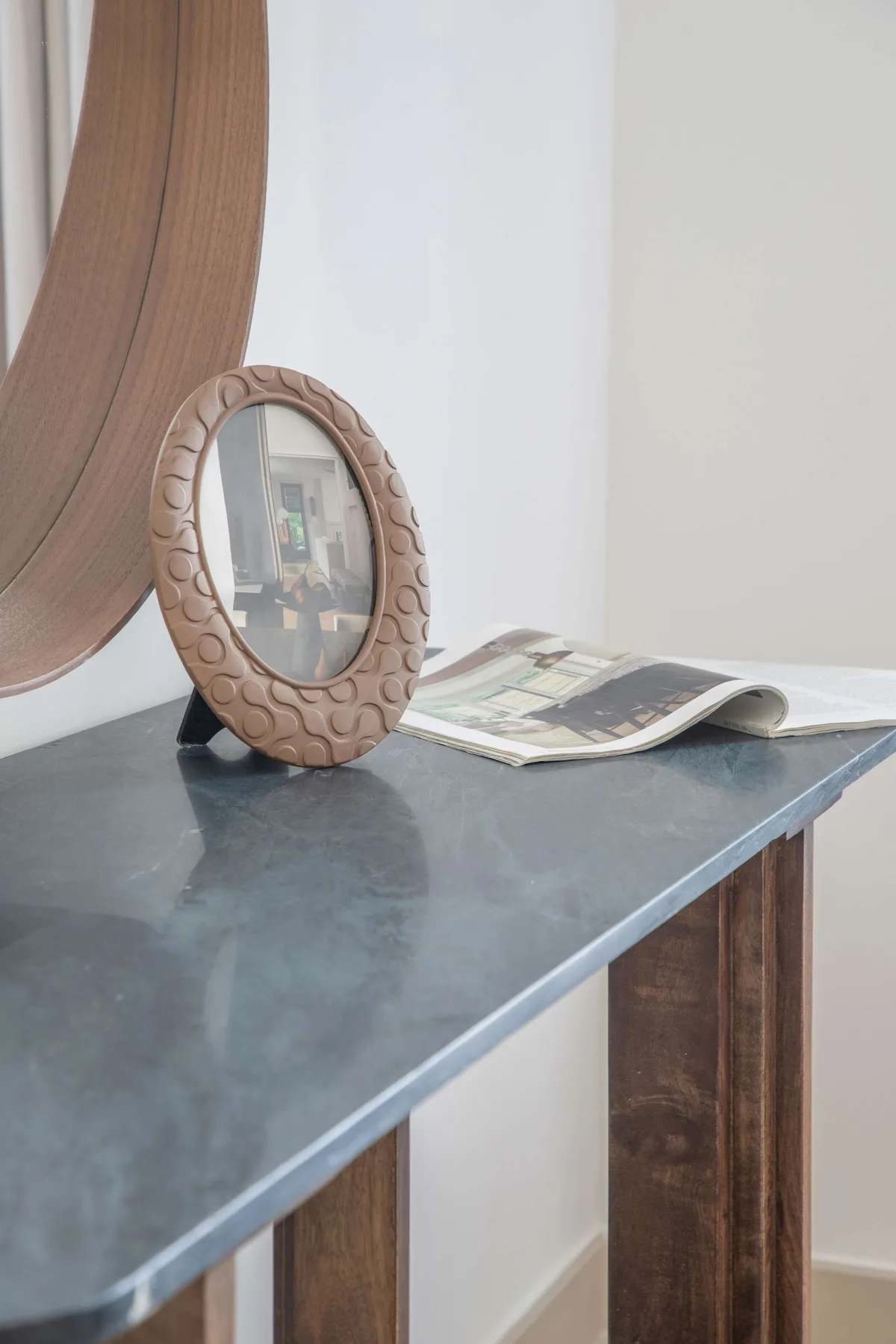 Una mesa consola estrecha exhibe un espejo ovalado y una revista abierta.