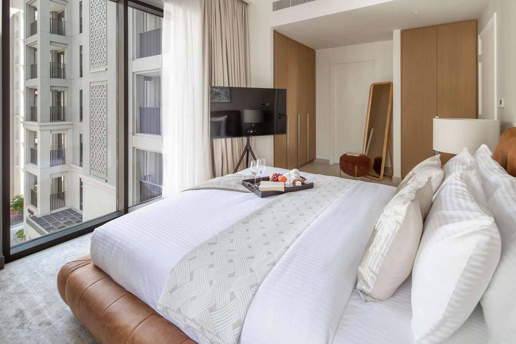 Un dormitorio luminoso con una cama grande junto a ventanales y un televisor.
