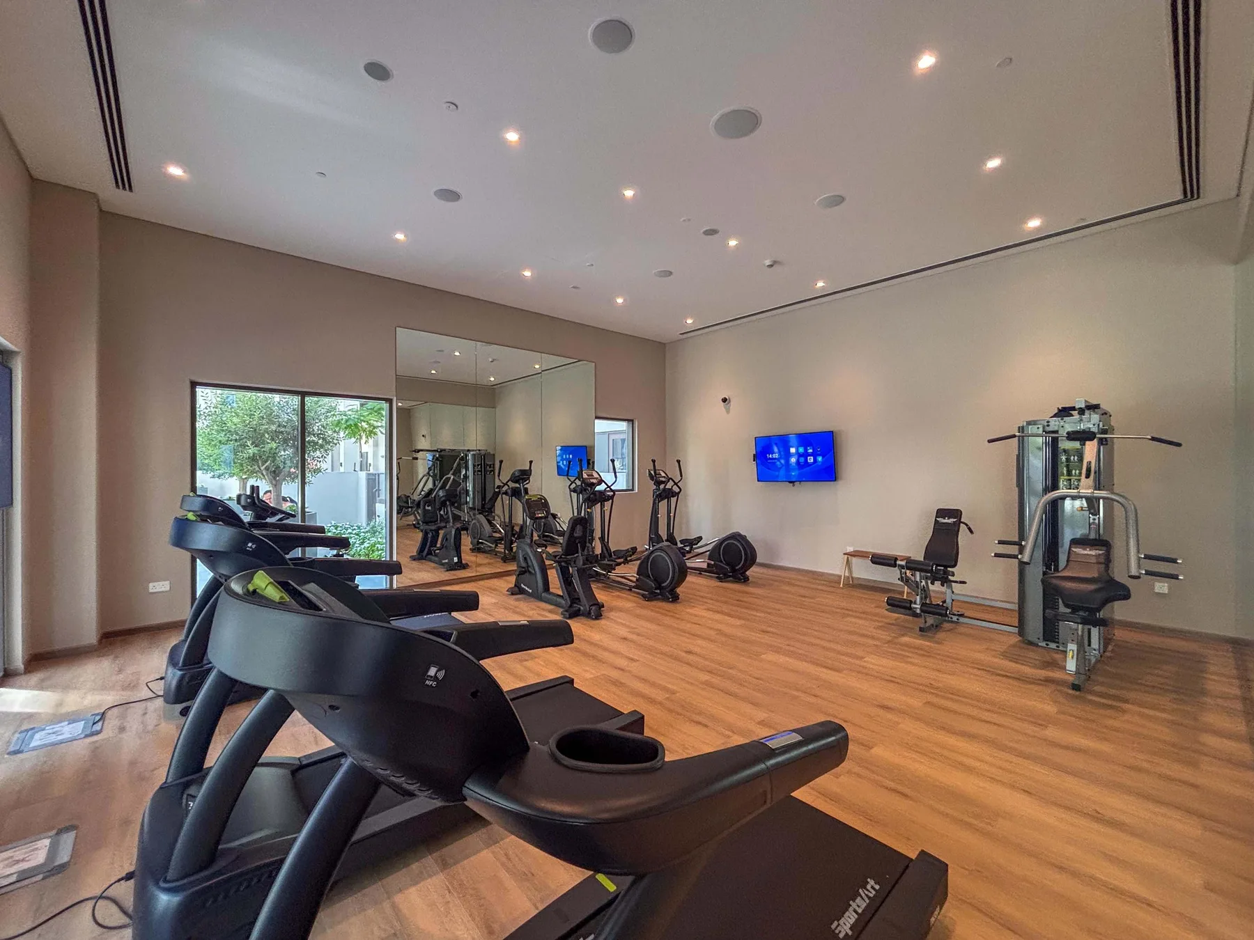 Una sala de ejercicio con cintas de correr y otros equipos sobre un suelo de madera.