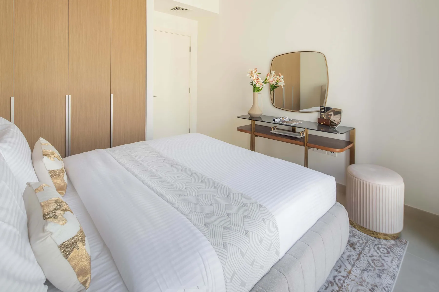 Un dormitorio luminoso con una cama bien tendida y un tocador con espejo.