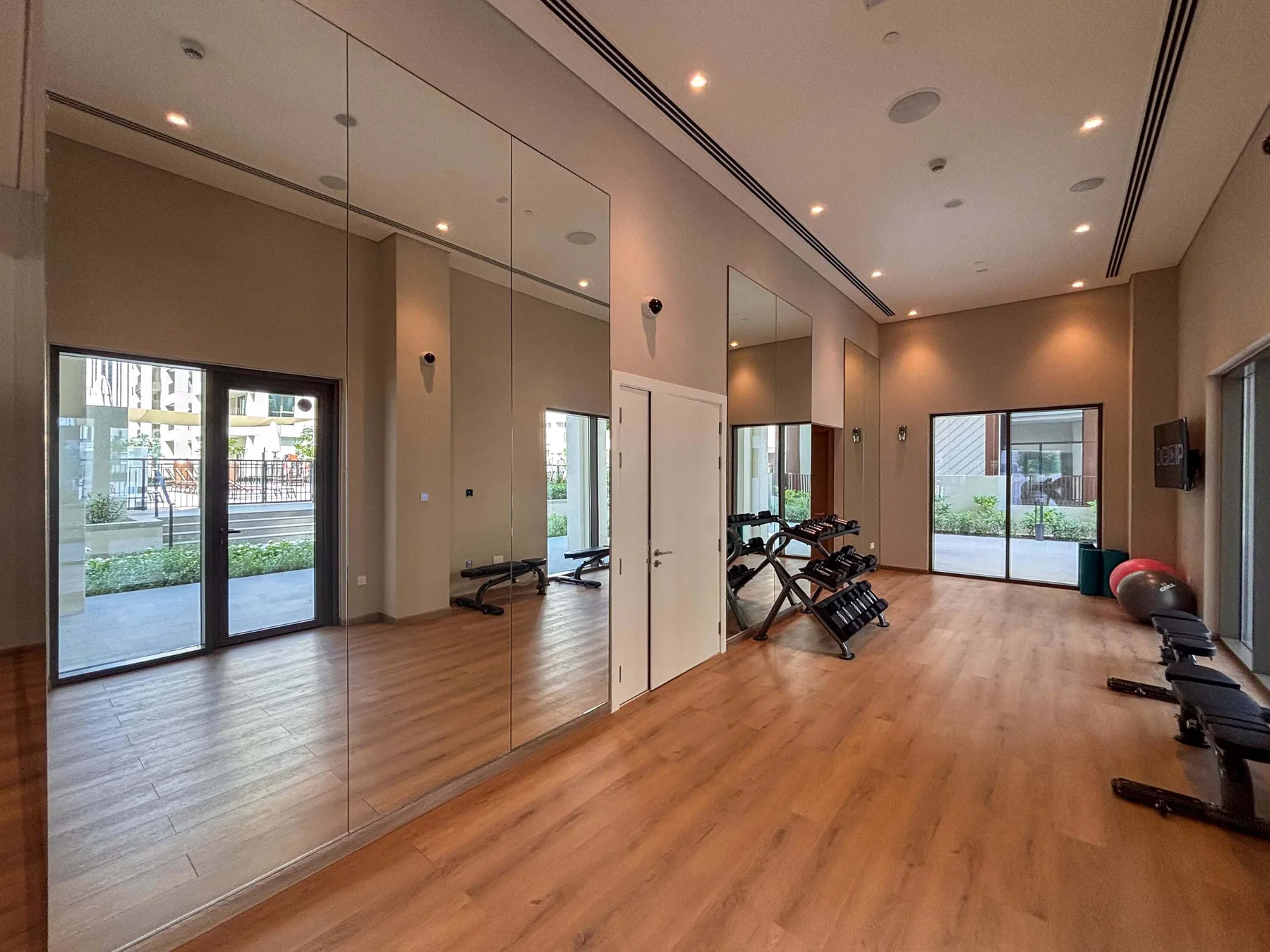 Una sala de ejercicio luminosa con paredes de espejo, equipo de entrenamiento y ventanales.