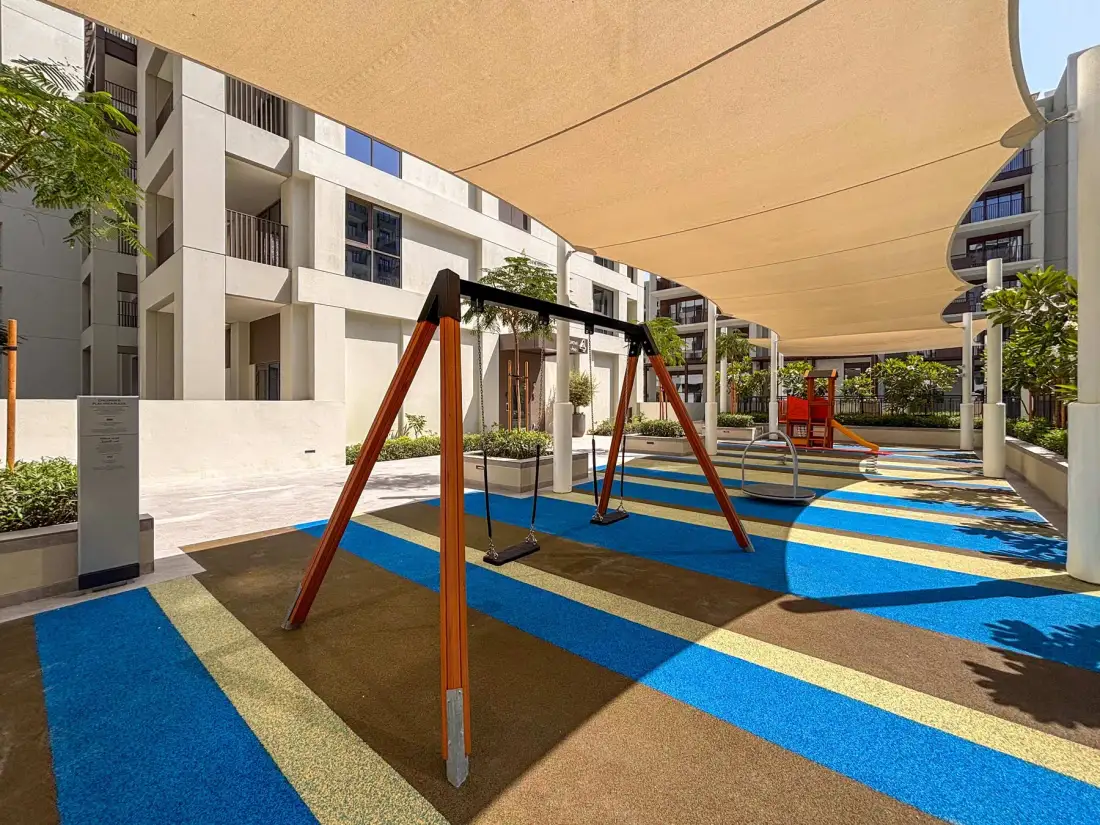 Un parque infantil al aire libre con columpios está bajo una gran cubierta de sombra.