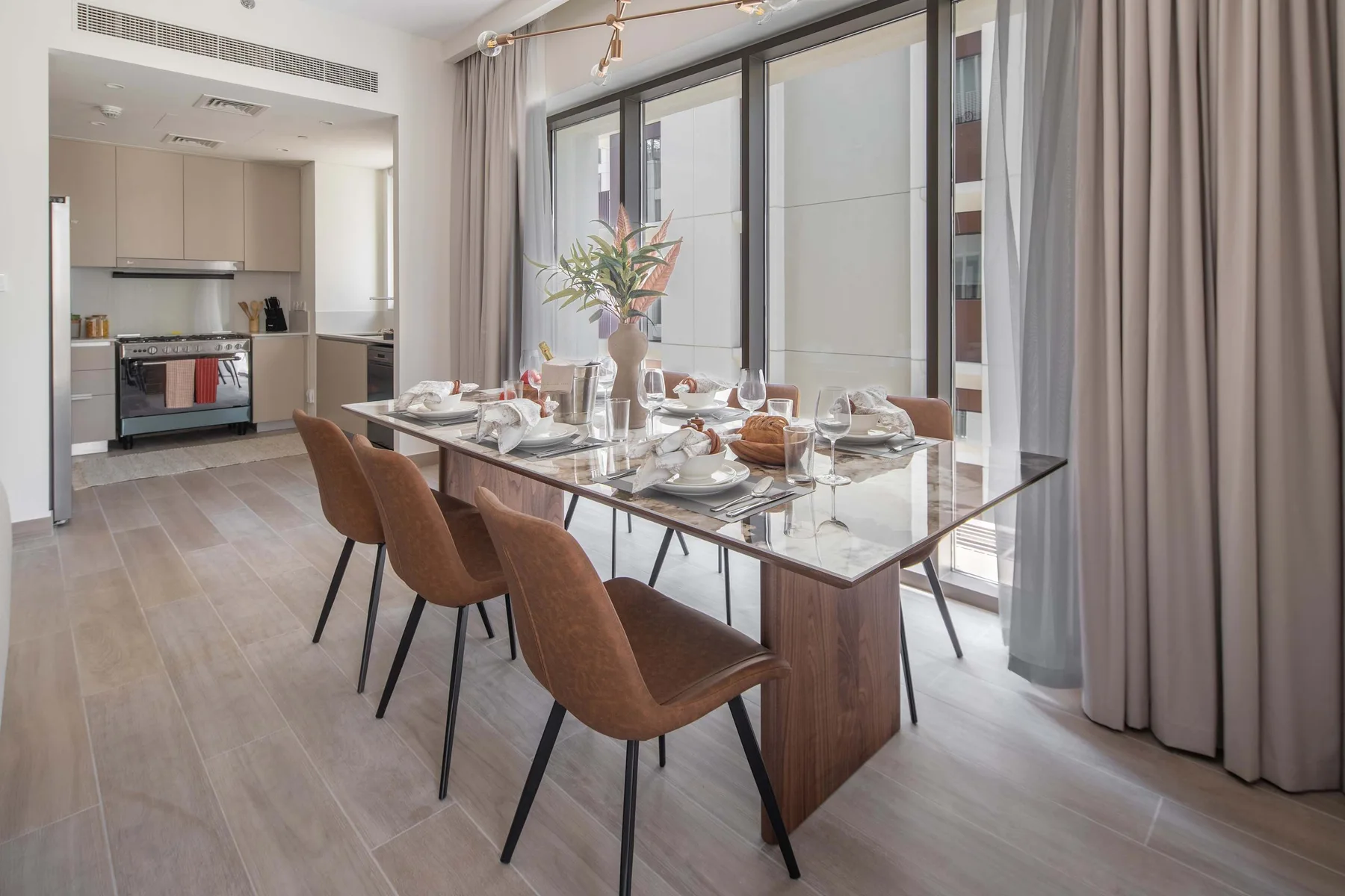Comedor con la mesa puesta junto a grandes ventanales y una cocina abierta.