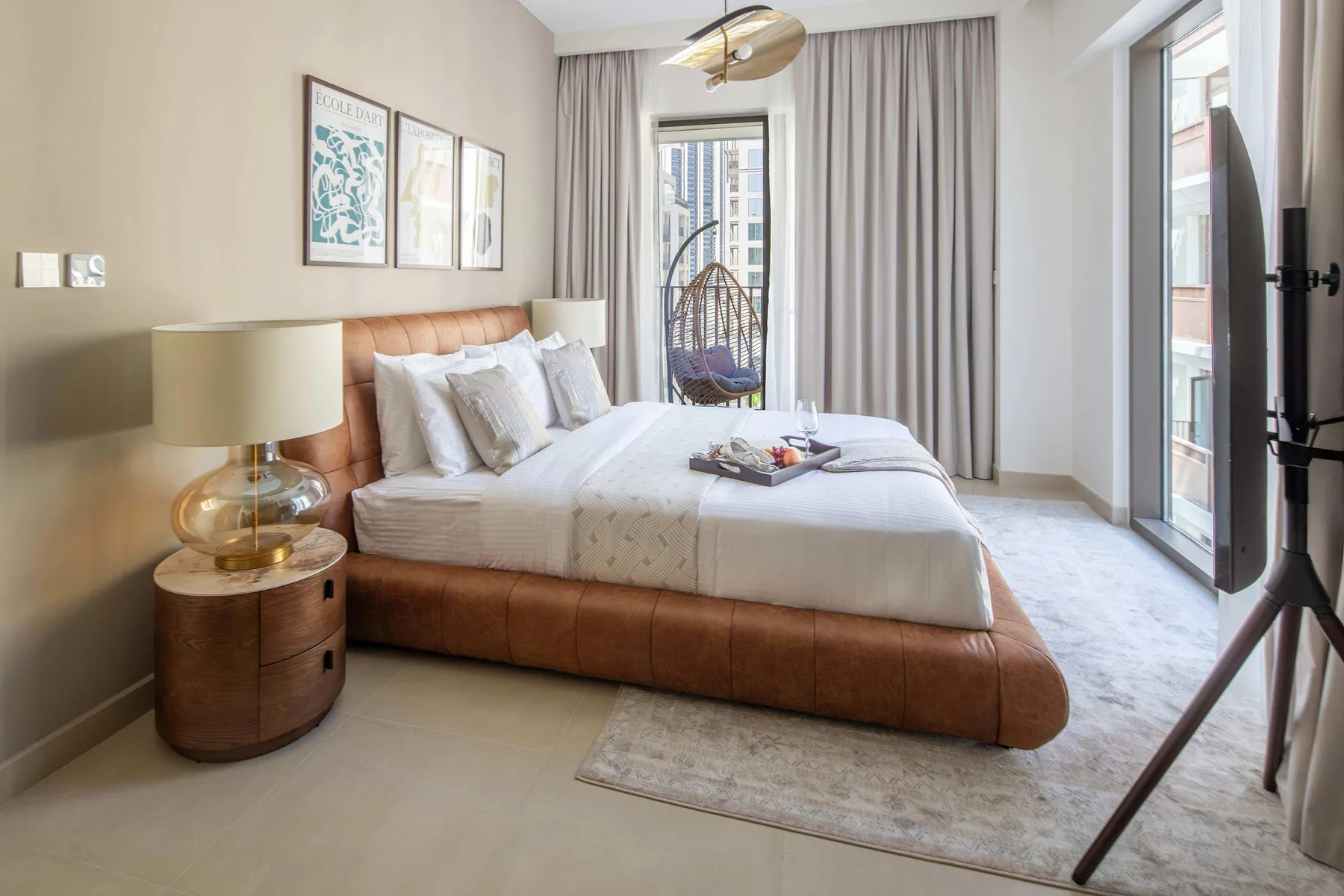 Un dormitorio luminoso con una cama grande, una mesita de noche y cortinas junto a las ventanas.
