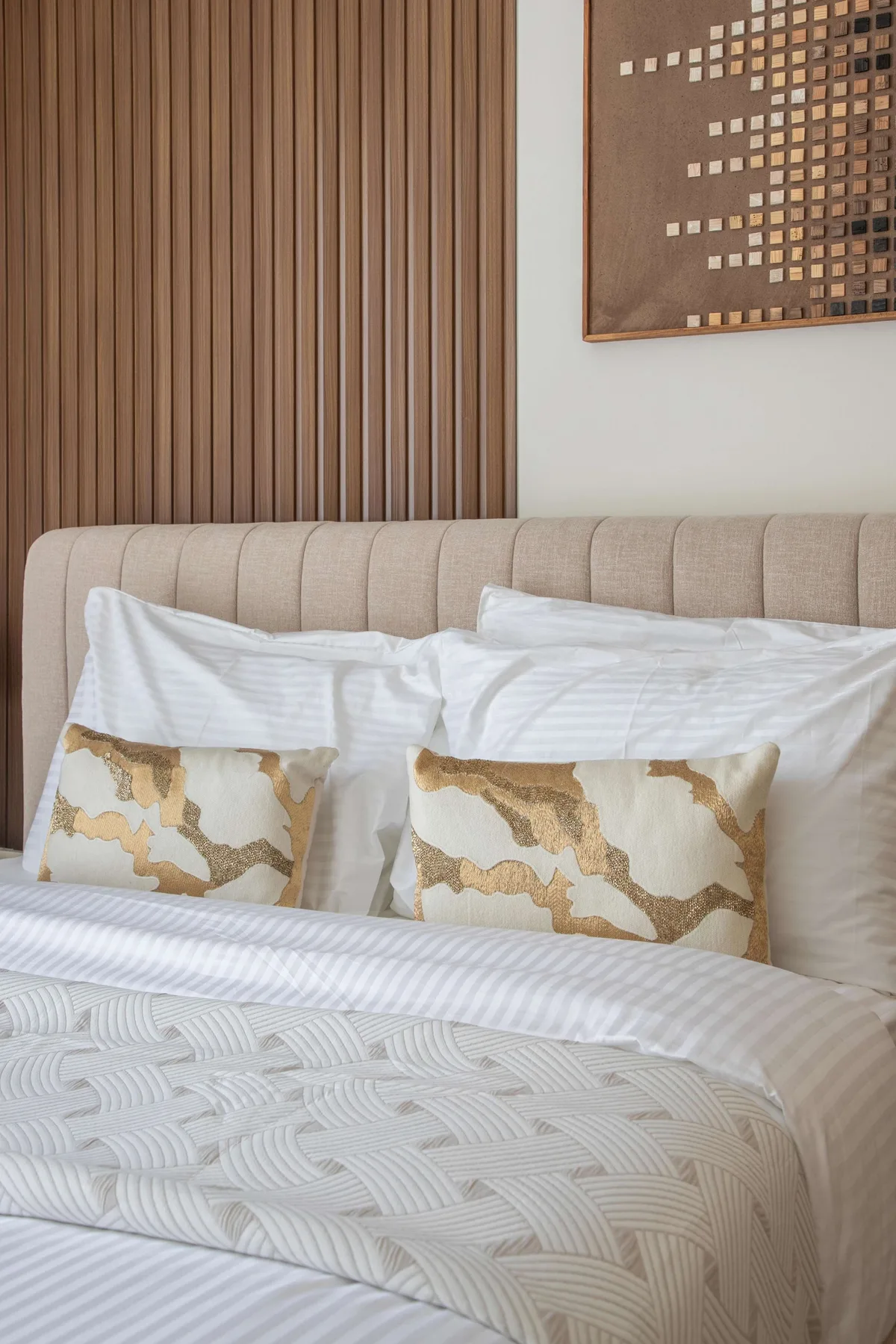 Una cama bien tendida con cojines estampados está frente a una pared con paneles.
