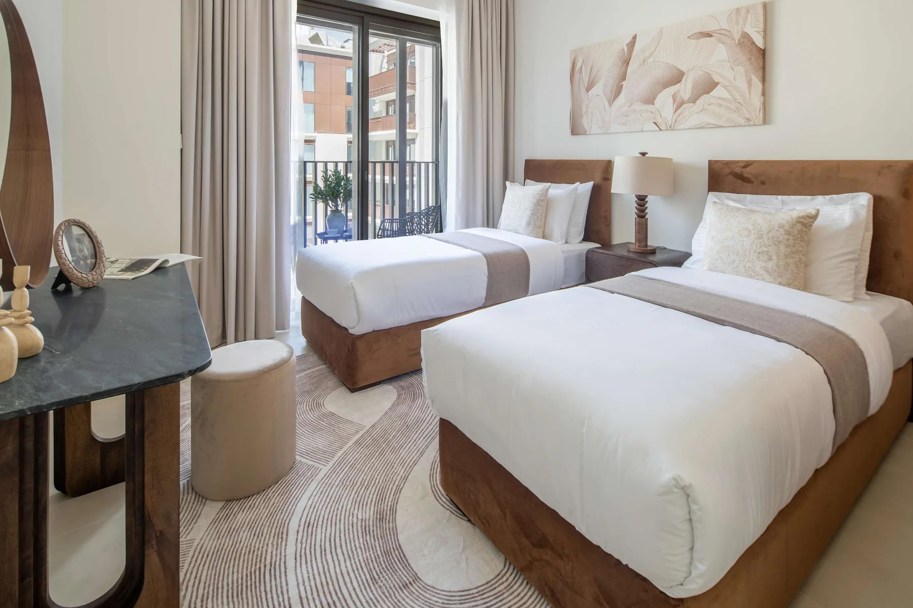 Un dormitorio luminoso con dos camas, una ventana y ropa de cama en tonos neutros.