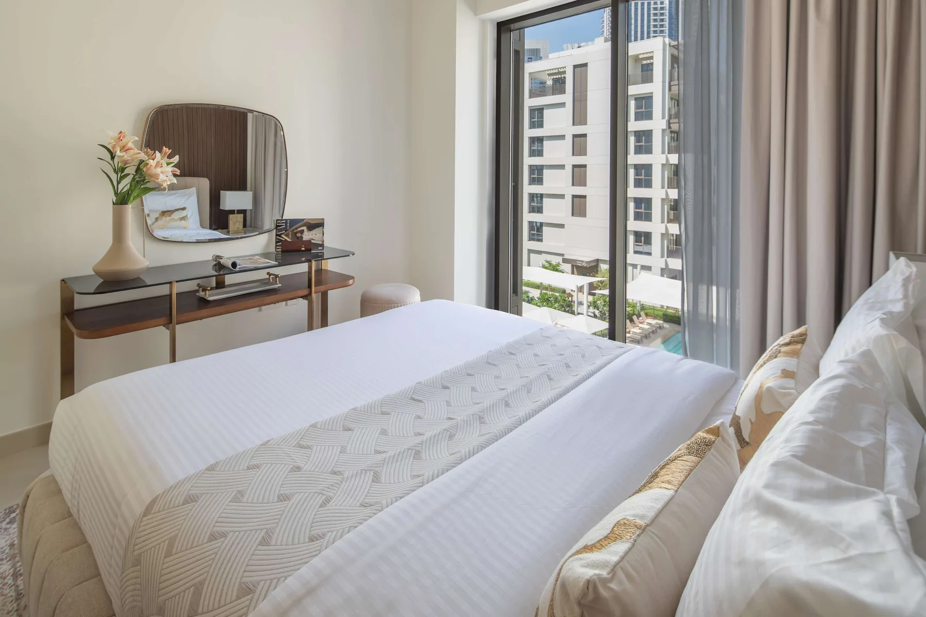 Un dormitorio con una cama bien tendida y una ventana amplia con edificios cercanos a la vista.