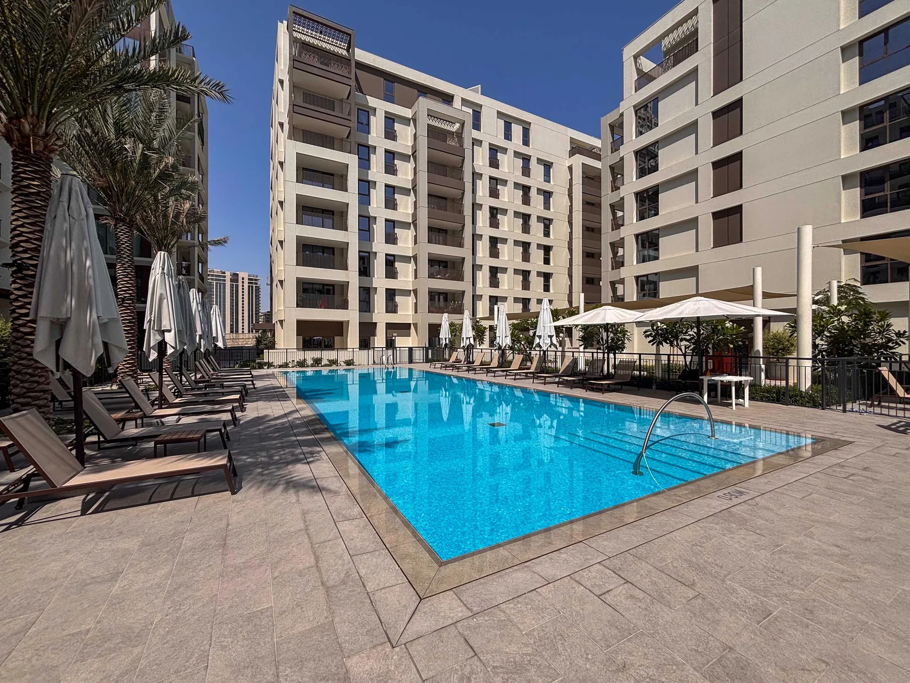 Una piscina al aire libre está rodeada de asientos de descanso y edificios modernos.