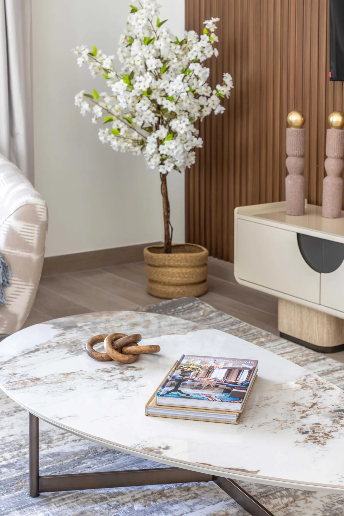 Sala de estar con un árbol en flor junto a un mueble bajo y una mesa de centro ovalada.