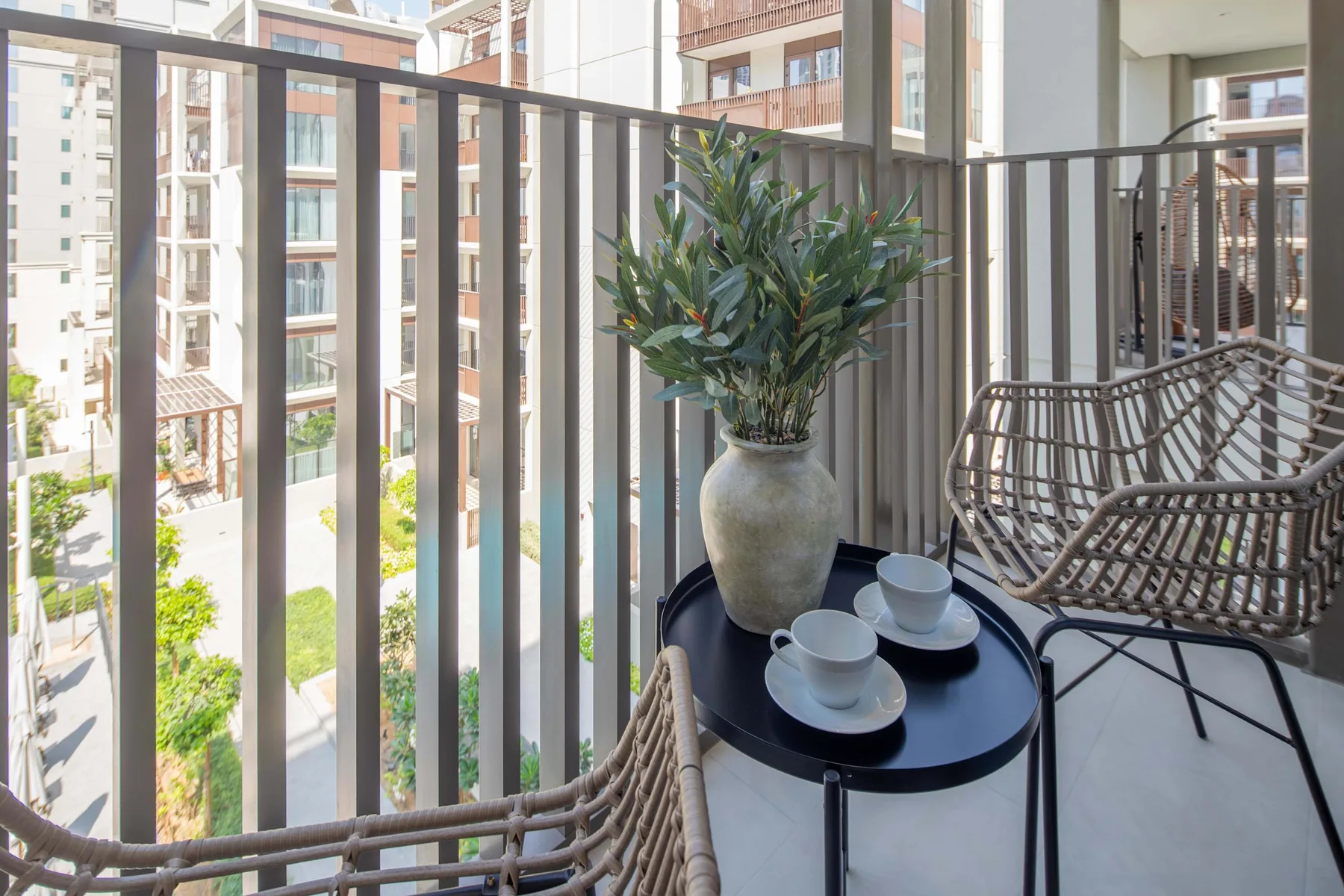 Una zona de estar en el balcón tiene una mesa pequeña, tazas y una planta en maceta.