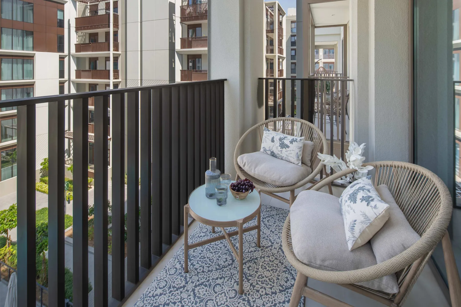 Un balcón amueblado con asientos y una mesita da a edificios de apartamentos cercanos.