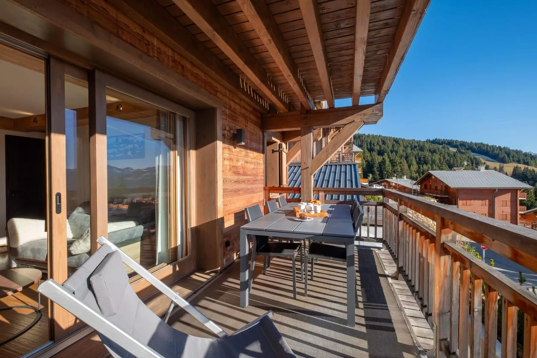 A covered balcony with outdoor seating overlooks wooded hills and nearby buildings.