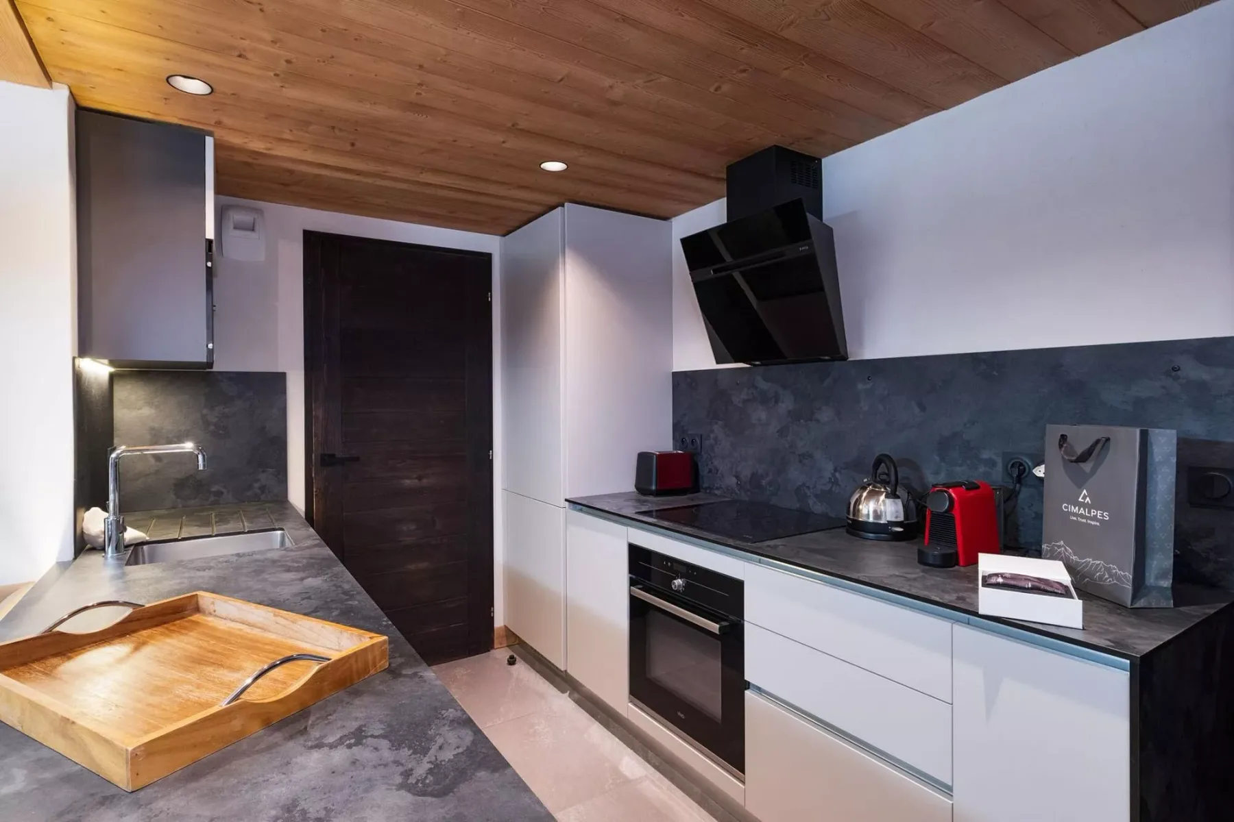 A modern kitchen with dark countertops and a wooden ceiling.