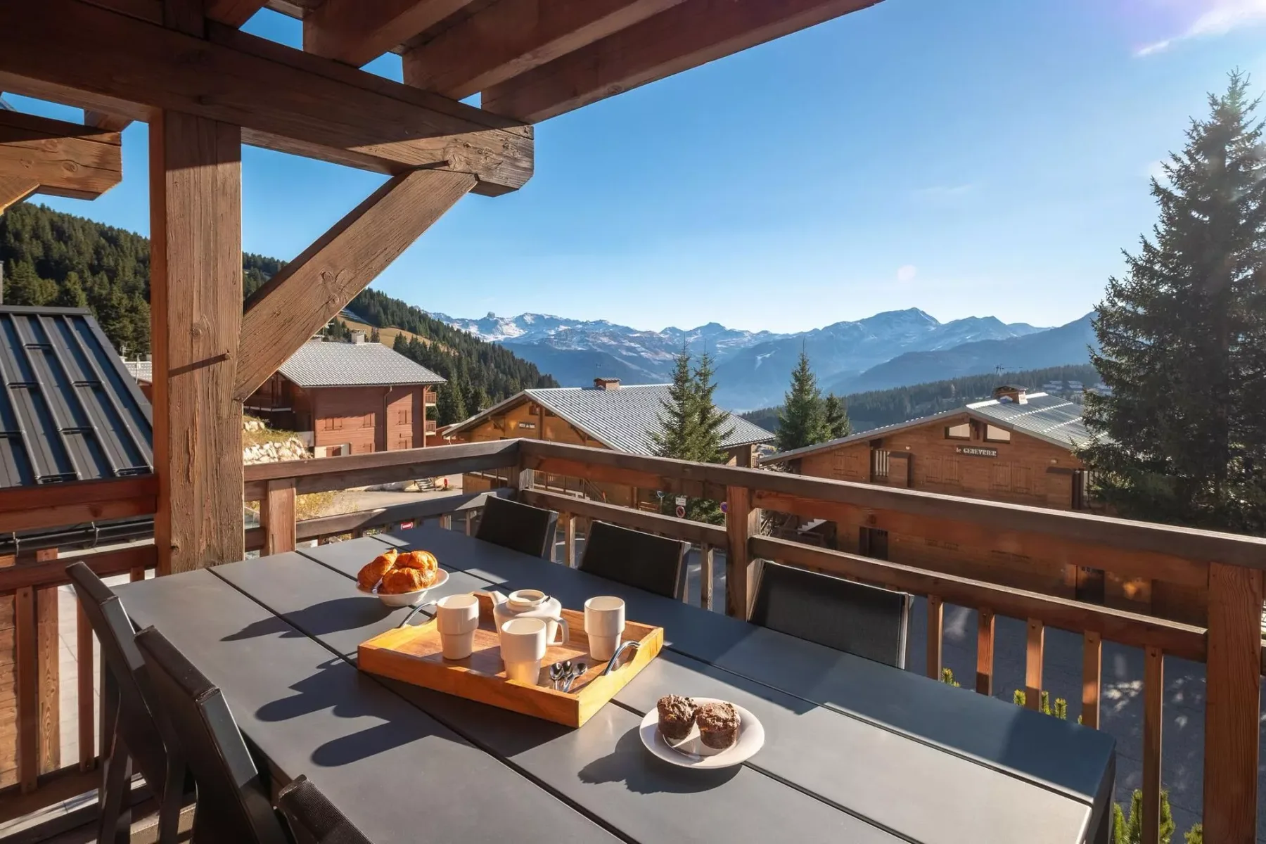 A wooden terrace with a dining table overlooks a mountain village.