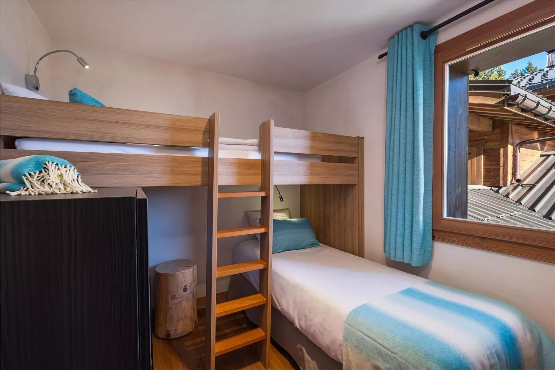 A bedroom with wooden bunk beds and a window overlooking nearby rooftops.