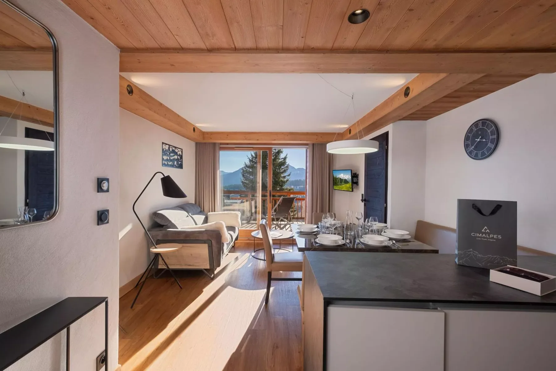 A bright open-plan living and dining area with a kitchen counter and mountain views.