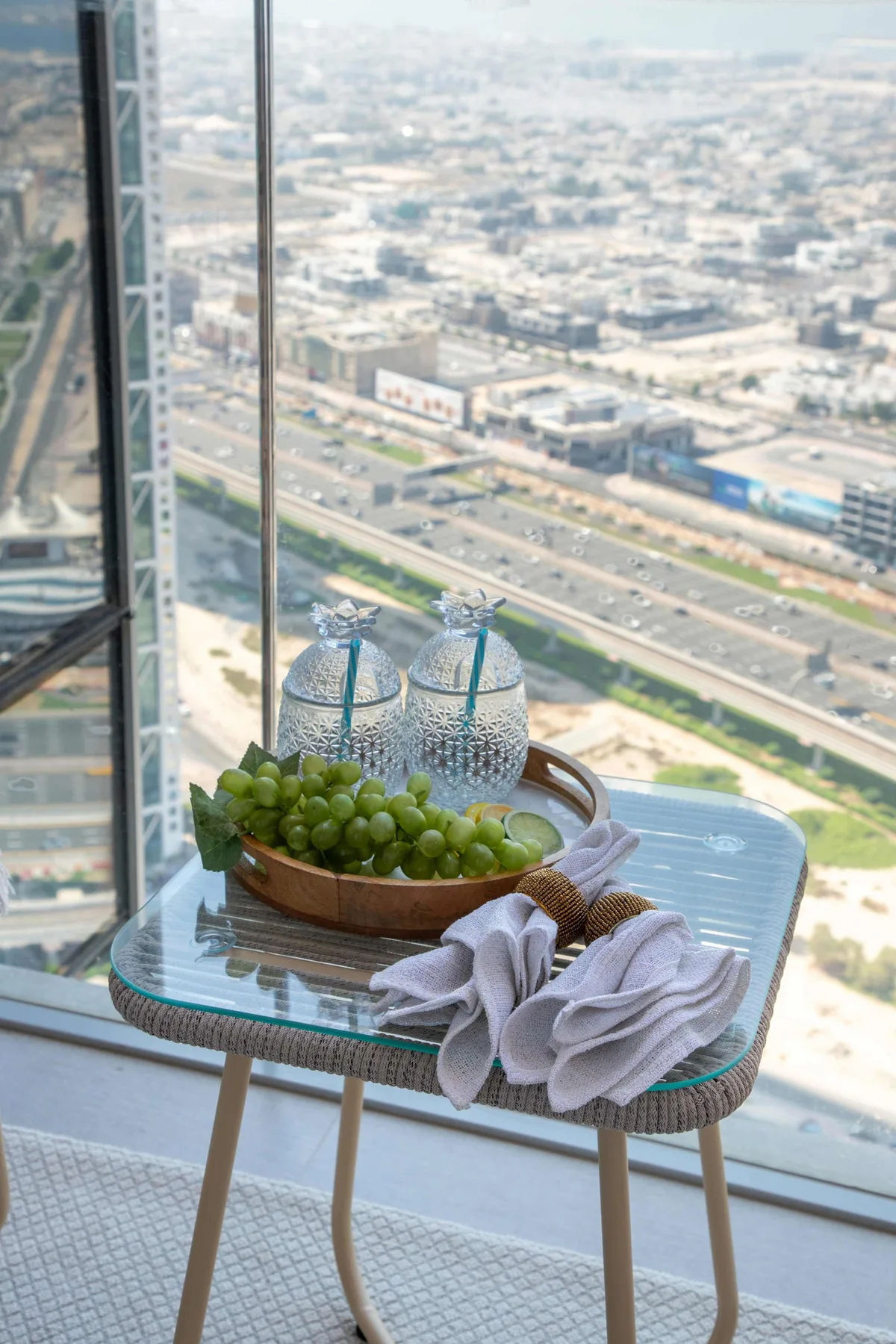 A small table by a floor-to-ceiling window holds a bowl of green grapes.