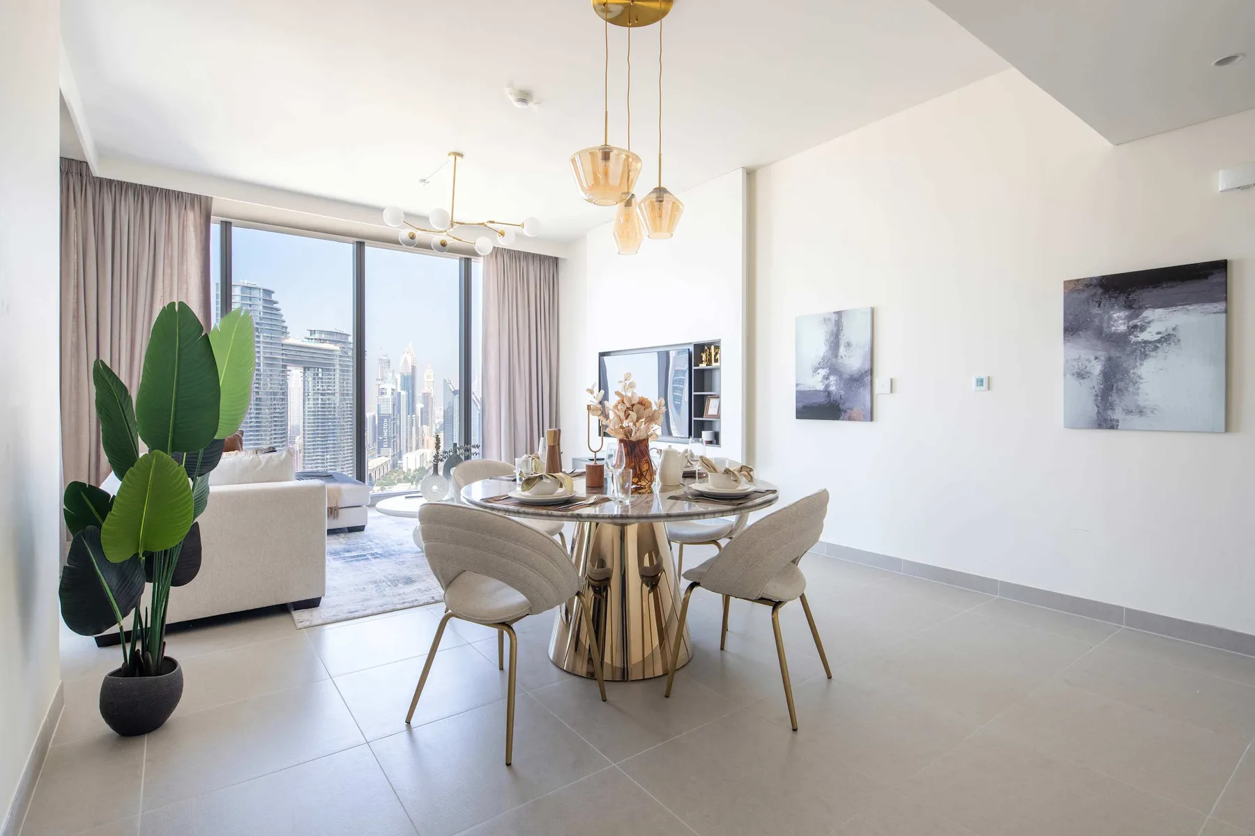 A bright dining and living area features a round table beside large windows.